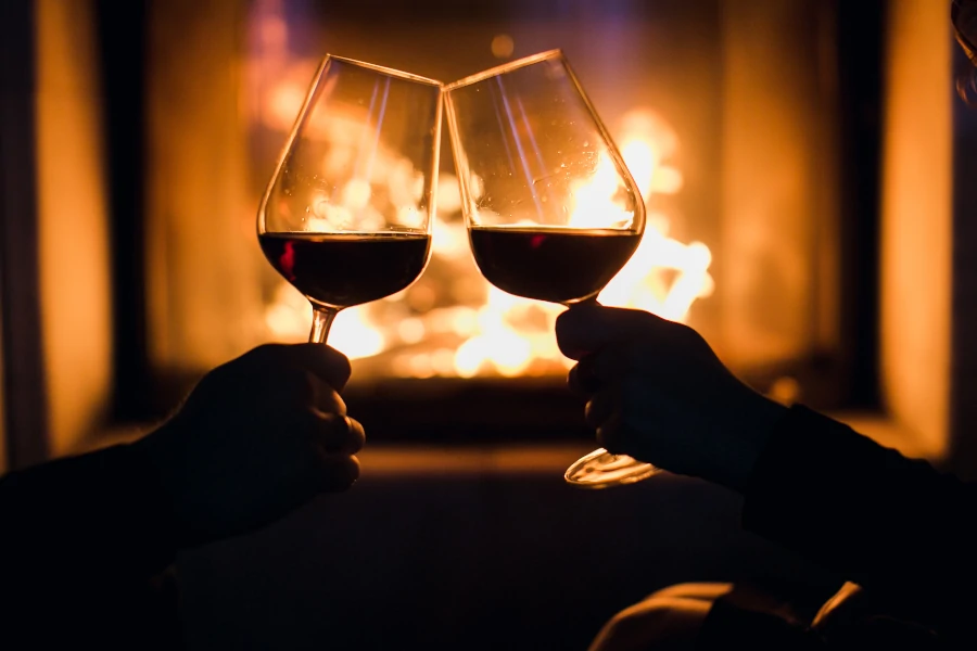 Couple toasting in front of fireplace with two glasses of red wine