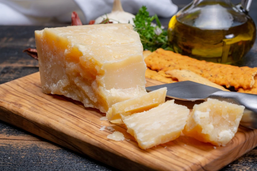 Aged Italian Parmesan cheese, Parmigiano Reggiano, with cut small pieces on wooden board