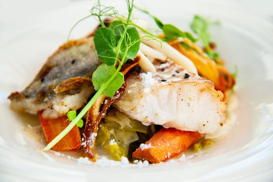 Delicious fillet of cod fish with carrots, leeks and mushrooms in white plate ready to be served