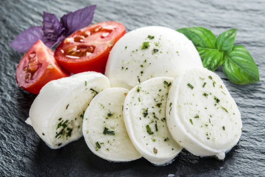 Mozzarella cheese with spices, tomatoes and basil leaves on a stone board