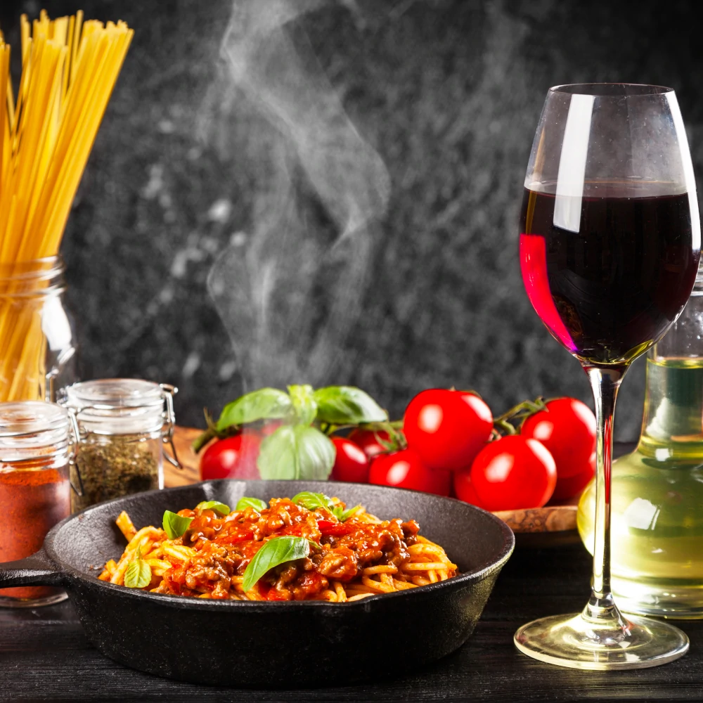 Pan with hot pasta with meat sauce and a glass of red wine
