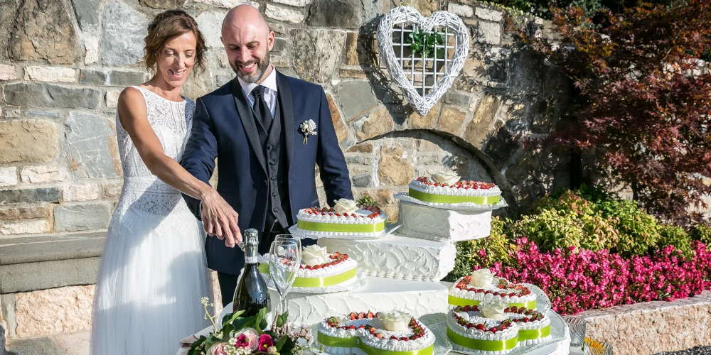 Bride and groom cutting wedding cake, bottle of wine and glasses