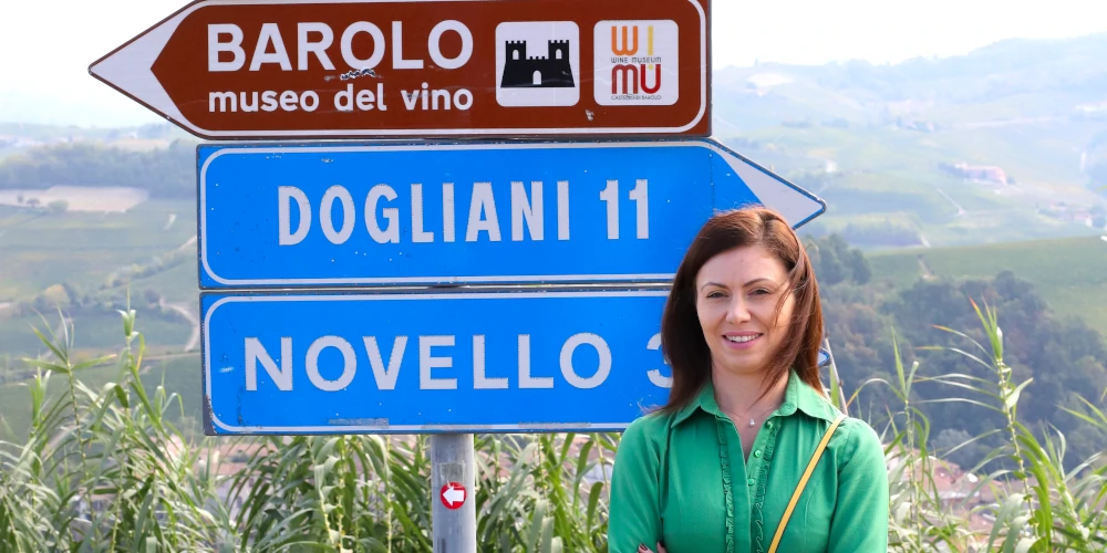 Elvira D, CEO of Independent Wine Ltd, standing in front of a road sign in Barolo